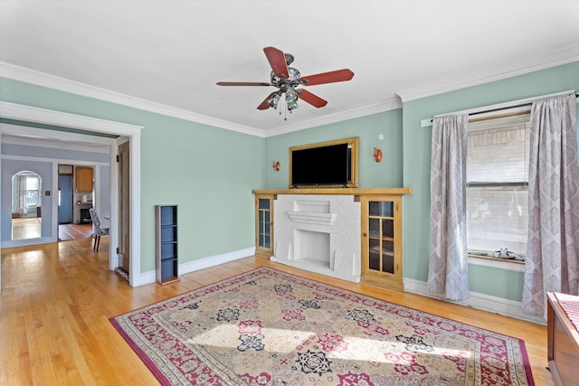 living room featuring crown molding, wood-type flooring, a fireplace, and ceiling fan