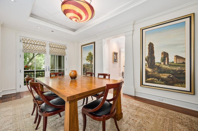 dining room featuring decorative columns, hardwood / wood-style flooring, ornamental molding, and a raised ceiling