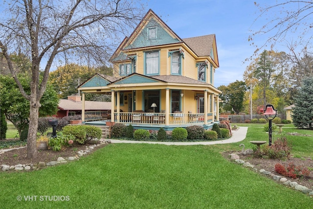 victorian home with covered porch, a front yard, and a shingled roof