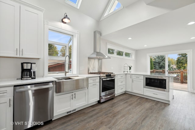 kitchen featuring wall chimney exhaust hood, white cabinets, stainless steel appliances, and kitchen peninsula