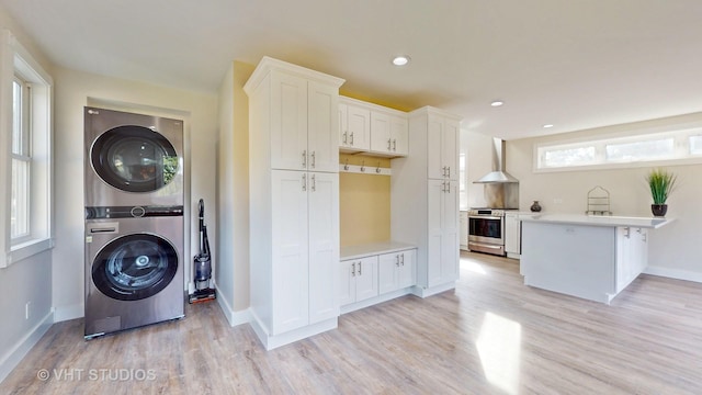laundry area featuring recessed lighting, laundry area, light wood-type flooring, baseboards, and stacked washing maching and dryer
