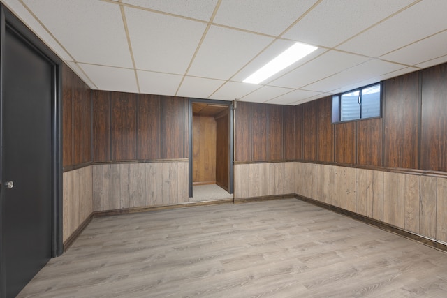 basement featuring light hardwood / wood-style floors, wooden walls, and a drop ceiling