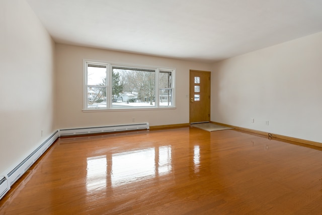 spare room featuring baseboard heating and light hardwood / wood-style floors