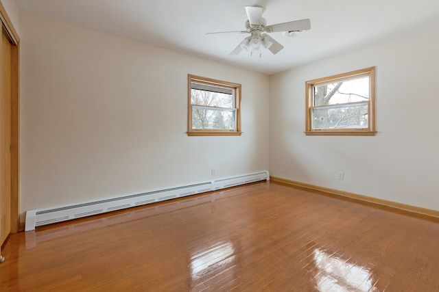 empty room with a baseboard heating unit, wood-type flooring, a healthy amount of sunlight, and ceiling fan