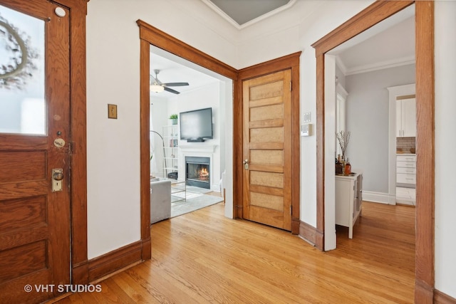 interior space featuring a lit fireplace, ornamental molding, light wood-style flooring, and baseboards