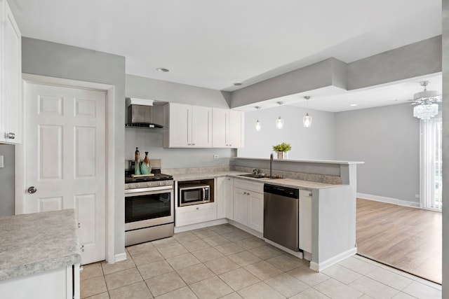 kitchen featuring wall chimney range hood, appliances with stainless steel finishes, kitchen peninsula, decorative light fixtures, and white cabinets