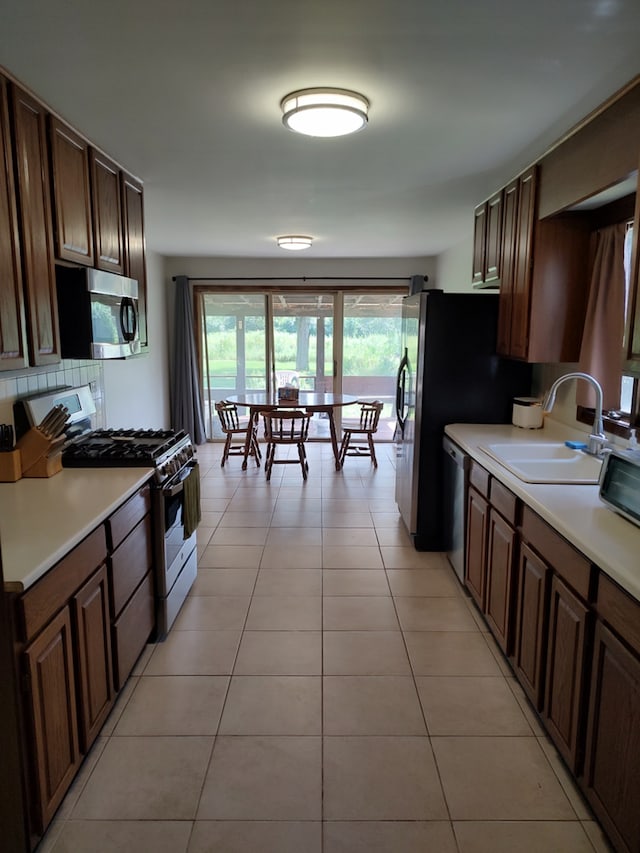 kitchen featuring decorative backsplash, dark brown cabinets, sink, light tile patterned floors, and appliances with stainless steel finishes