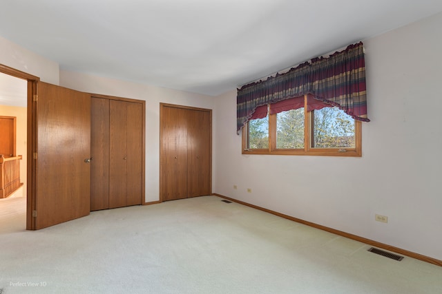 unfurnished bedroom with multiple closets and light colored carpet