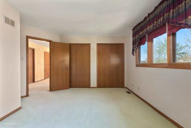 unfurnished bedroom with multiple closets and light colored carpet