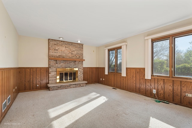 unfurnished living room featuring wooden walls, a fireplace, and light colored carpet