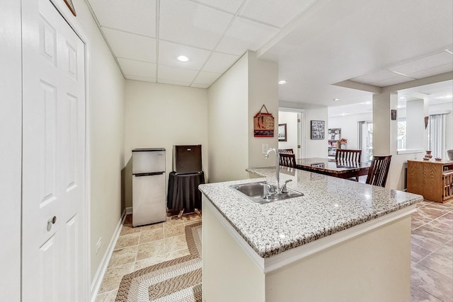 kitchen with light stone counters, sink, an island with sink, and a drop ceiling