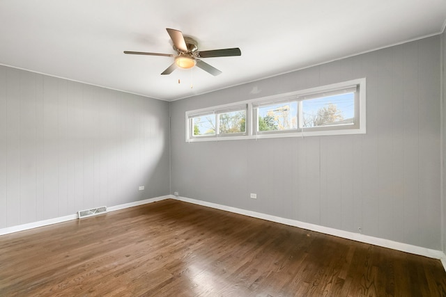 spare room featuring hardwood / wood-style floors, ceiling fan, and wooden walls