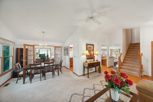 dining space featuring light carpet, a healthy amount of sunlight, ceiling fan with notable chandelier, and vaulted ceiling