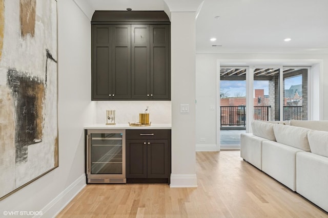 bar with backsplash, wine cooler, light wood-type flooring, ornamental molding, and dark brown cabinets