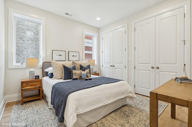 bedroom with light hardwood / wood-style floors, multiple windows, and two closets