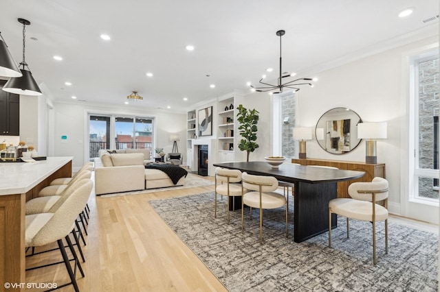 dining room with built in features, light wood-type flooring, crown molding, and an inviting chandelier