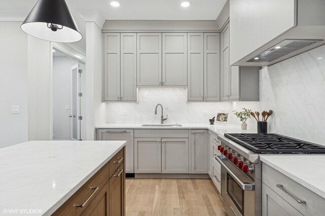 kitchen featuring light stone countertops, sink, high end stainless steel range oven, and light hardwood / wood-style flooring