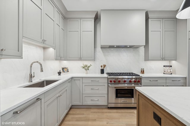 kitchen with light stone counters, sink, luxury stove, and tasteful backsplash