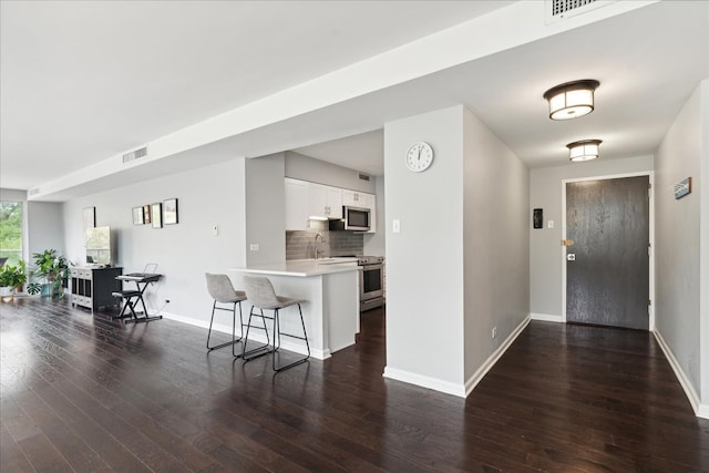 kitchen featuring a kitchen breakfast bar, dark wood-type flooring, kitchen peninsula, white cabinets, and appliances with stainless steel finishes