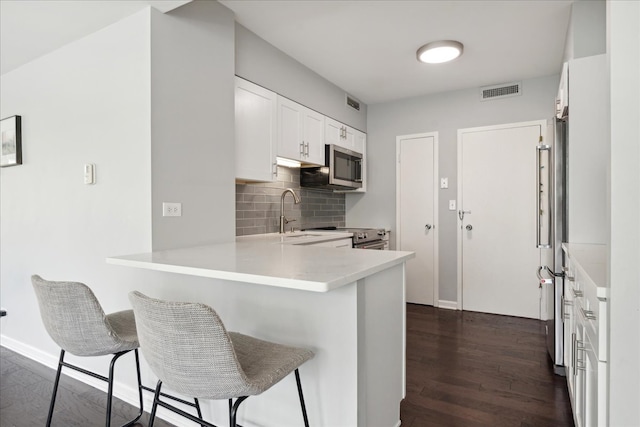 kitchen with kitchen peninsula, stainless steel appliances, white cabinets, a breakfast bar, and dark hardwood / wood-style floors