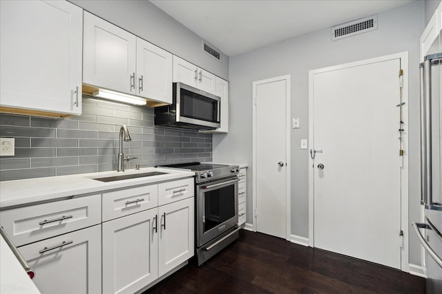 kitchen featuring white cabinets, backsplash, dark wood-type flooring, sink, and stainless steel appliances