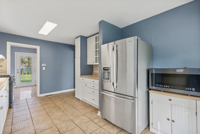 kitchen with stainless steel appliances, white cabinetry, light tile patterned floors, and tasteful backsplash