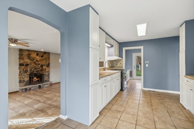 kitchen featuring a fireplace, light tile patterned flooring, stove, and white cabinets