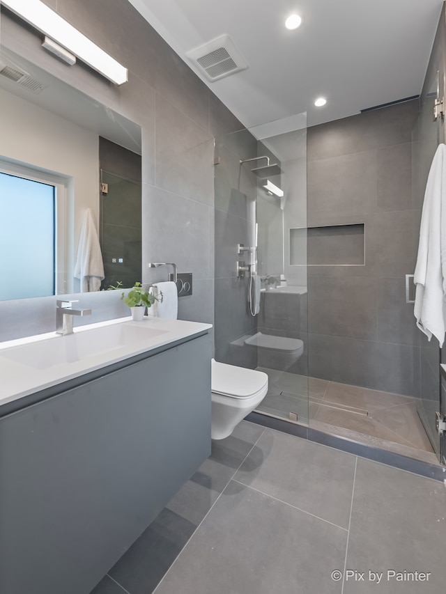 bathroom featuring toilet, tile walls, tiled shower, vanity, and tile patterned flooring