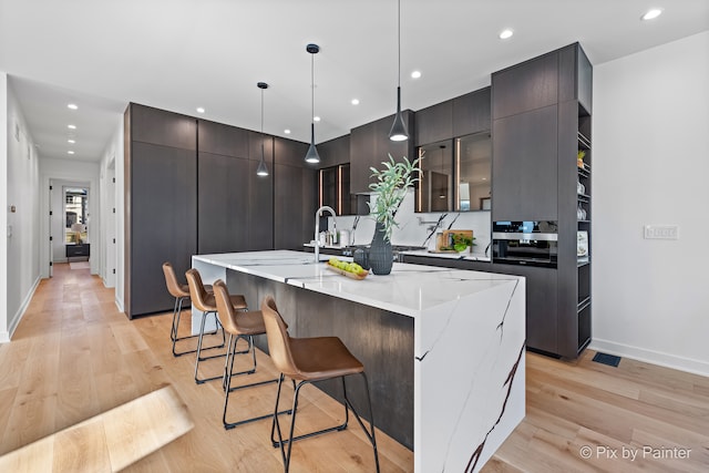 kitchen with a large island, a kitchen bar, light wood-type flooring, and hanging light fixtures