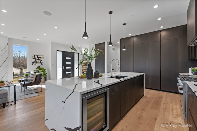 kitchen featuring wine cooler, light hardwood / wood-style flooring, decorative light fixtures, and an island with sink