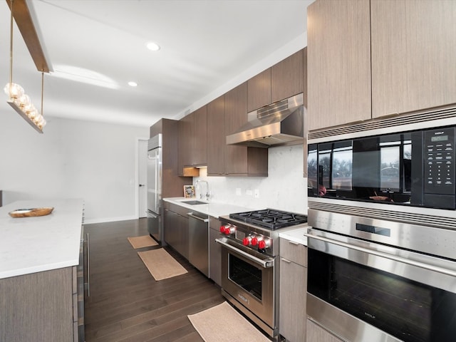 kitchen featuring dark hardwood / wood-style flooring, backsplash, high end appliances, sink, and decorative light fixtures