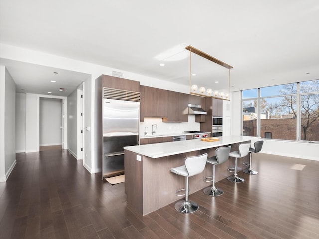 kitchen featuring sink, pendant lighting, built in appliances, a center island, and dark hardwood / wood-style floors