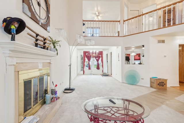 interior space with carpet flooring, a fireplace, a towering ceiling, and ceiling fan with notable chandelier