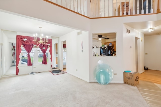 carpeted entrance foyer featuring ceiling fan with notable chandelier and a high ceiling