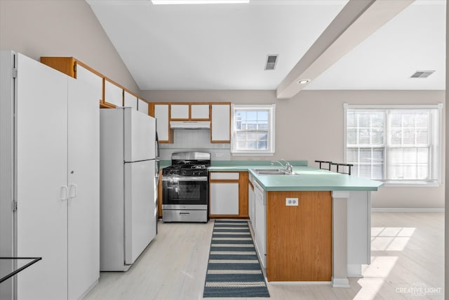 kitchen featuring sink, stainless steel gas stove, light hardwood / wood-style floors, lofted ceiling, and white refrigerator