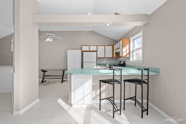 kitchen featuring kitchen peninsula, a kitchen breakfast bar, light wood-type flooring, vaulted ceiling, and white refrigerator