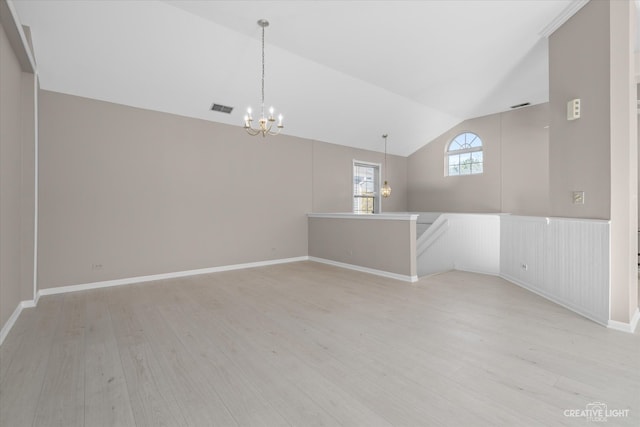 empty room featuring an inviting chandelier, vaulted ceiling, and light wood-type flooring