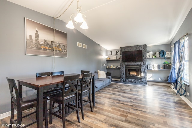 dining space with wood-type flooring, vaulted ceiling, a chandelier, and a fireplace