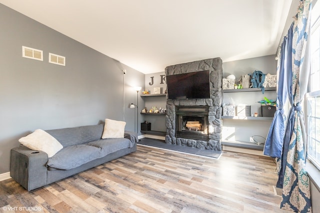 living room featuring lofted ceiling, a stone fireplace, and wood-type flooring