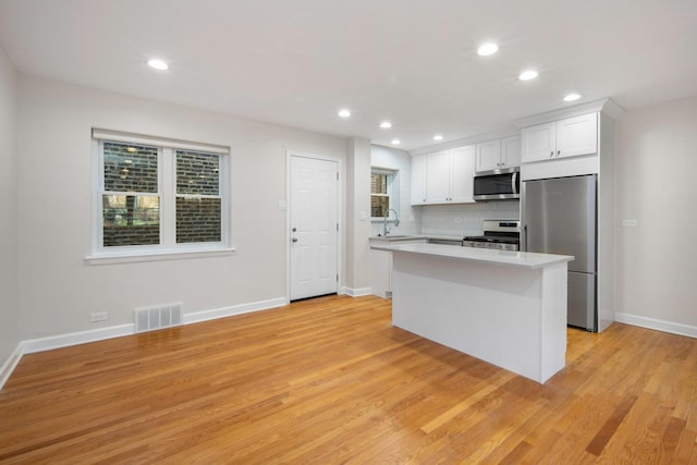 kitchen featuring sink, white cabinets, decorative backsplash, a center island, and stainless steel appliances