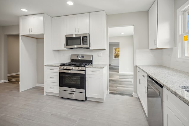 kitchen featuring appliances with stainless steel finishes, light stone counters, a healthy amount of sunlight, and white cabinets