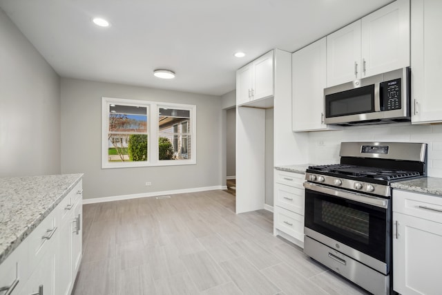 kitchen with white cabinetry, light stone counters, appliances with stainless steel finishes, and decorative backsplash