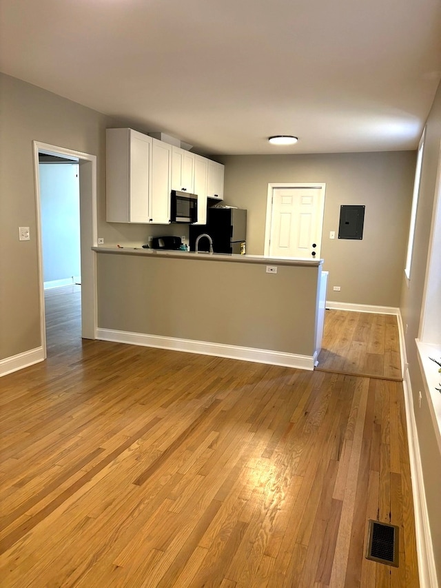 kitchen featuring sink, light wood-type flooring, refrigerator, white cabinets, and electric panel