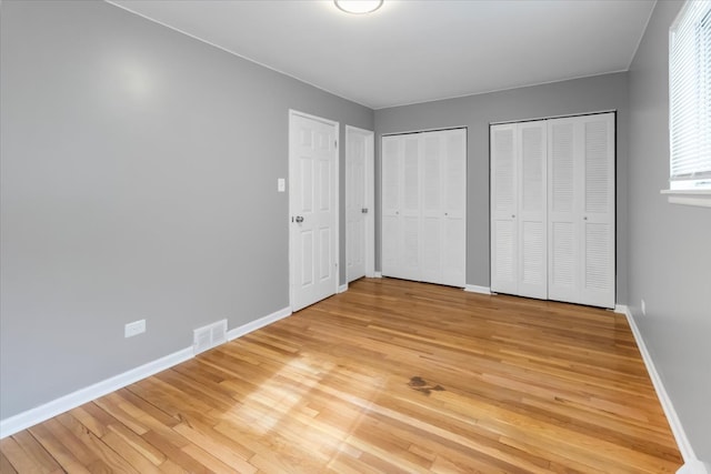 unfurnished bedroom with two closets and hardwood / wood-style floors