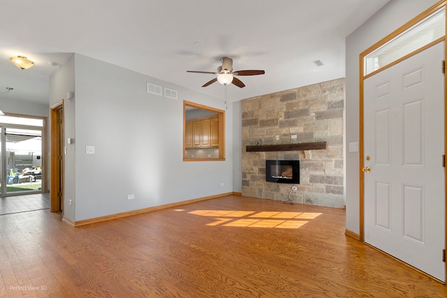 unfurnished living room featuring light hardwood / wood-style flooring, a stone fireplace, and ceiling fan