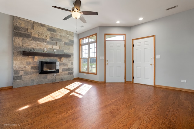 unfurnished living room featuring hardwood / wood-style floors, a stone fireplace, and ceiling fan