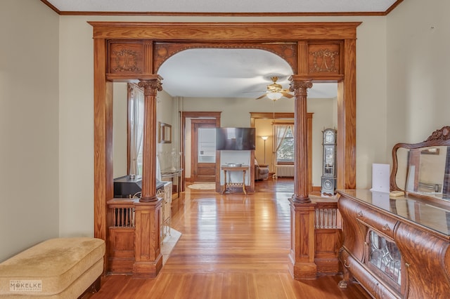 corridor with light wood-type flooring, radiator heating unit, ornate columns, and crown molding