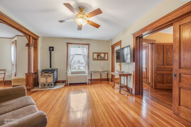 living area featuring radiator heating unit, a wood stove, ceiling fan, and light hardwood / wood-style flooring