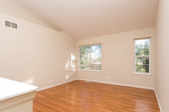 spare room featuring a healthy amount of sunlight, lofted ceiling, and hardwood / wood-style floors