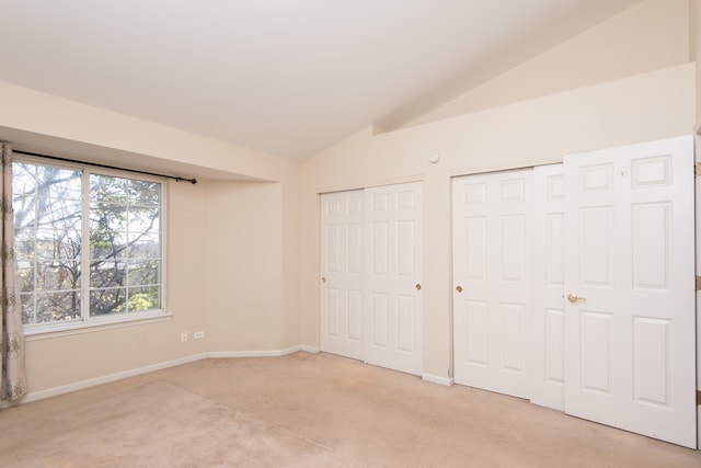 unfurnished bedroom with lofted ceiling, two closets, and light colored carpet